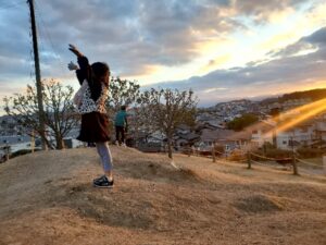 シーメイトの子ども公園横にある丘で、お子様が夕陽に背を向けている写真。